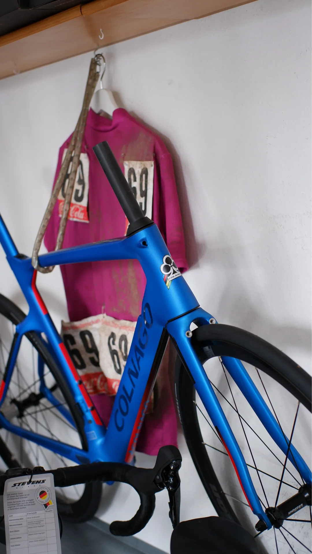 Blaues Colnago-Rennrad vor historischen Renntrikots
